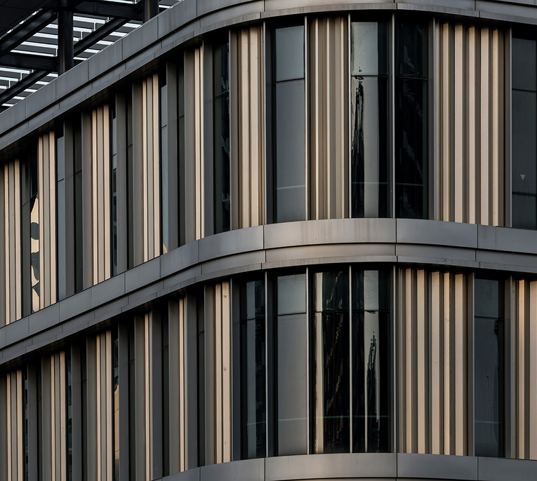 Contemporary office building façade with curved architecture, glass windows, and vertical metal fins.