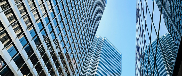 Modern glass office towers viewed from street level against a clear blue sky.